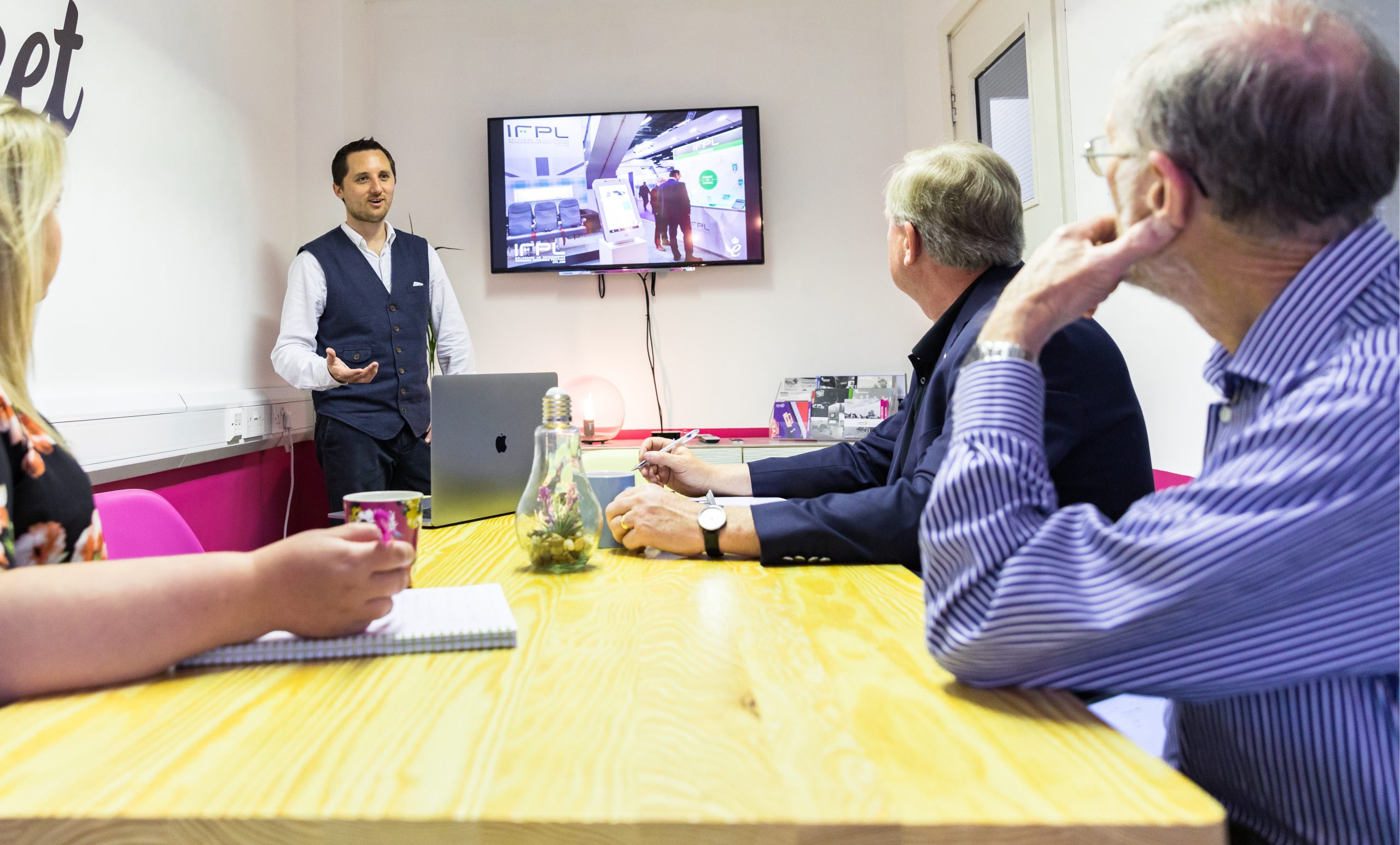 A man giving a presentation in front of a screen to a few people in an office space.