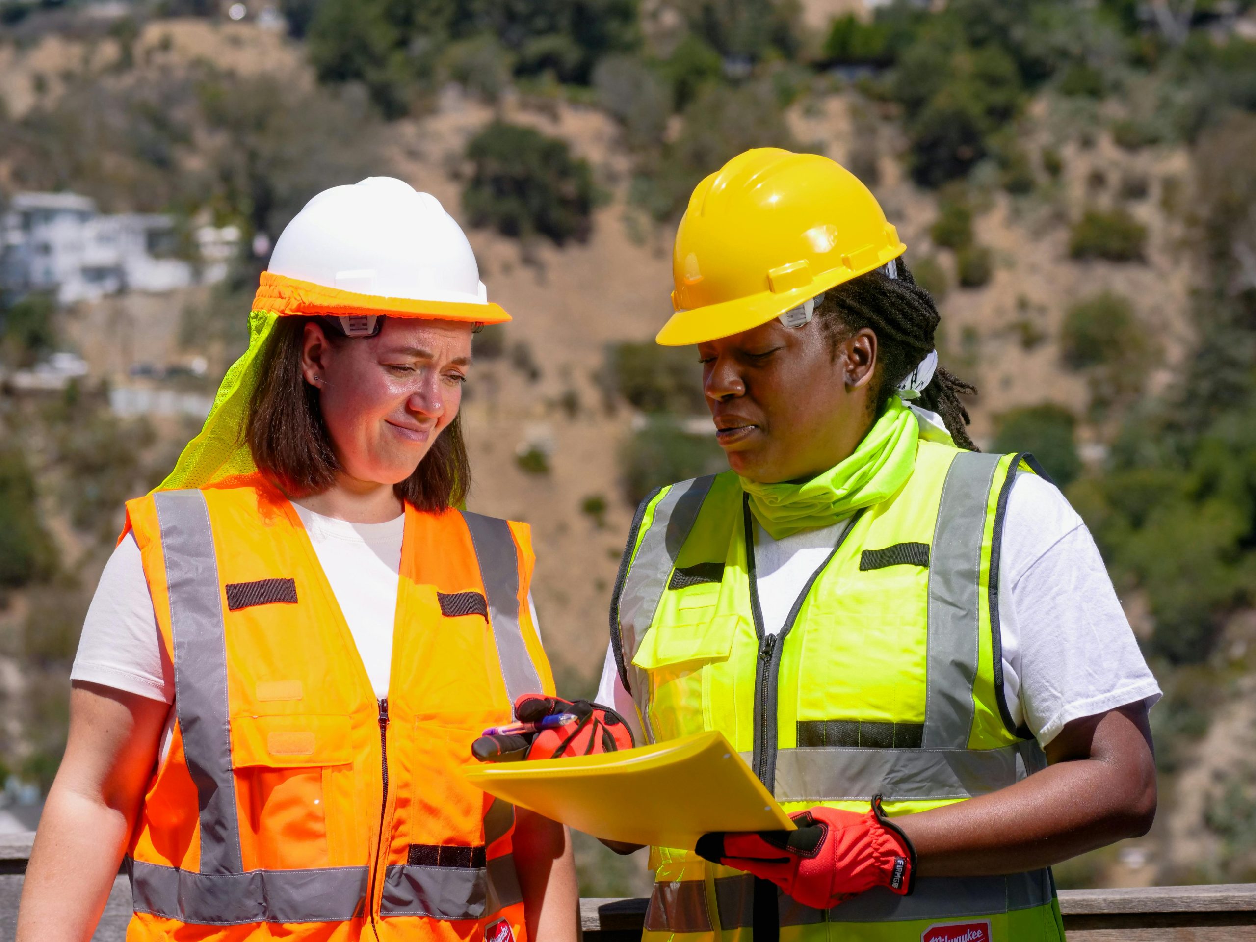 Two people at a building site wearing hard hats and high visibility protective clothing.