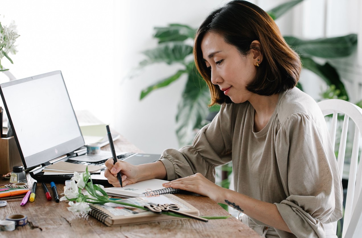 Business for creatives - a woman writing at a desk with pains and painbrushes